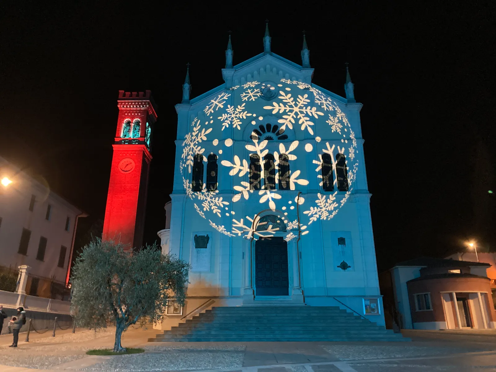 Fiocchi di neve proiettati sulla facciata di una chiesa, con il campanile illuminato di rosso, di notte per il Natale