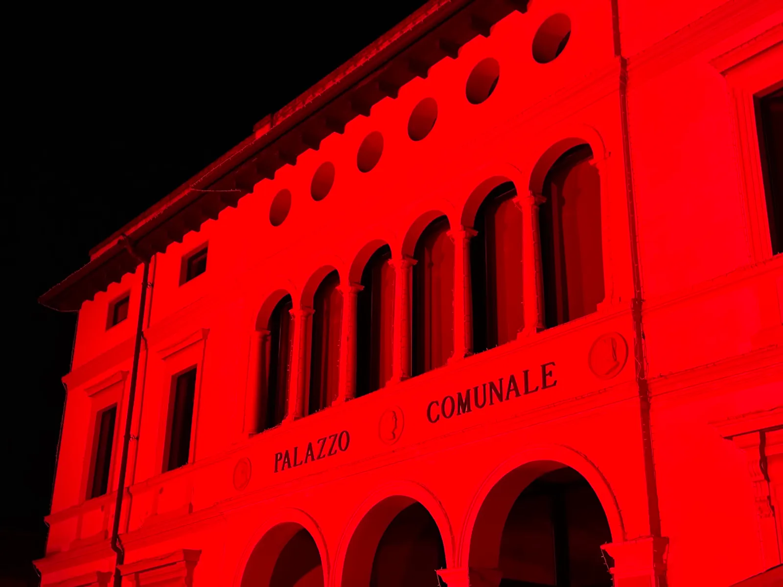 Palazzo comunale di Scanzorosciate interamente illuminato di rosso di notte, illuminazione a colori senza gobo, per il 25 novembre 2023